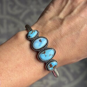 May include: Silver cuff bracelet featuring five oval turquoise stones. Each stone is a light blue color with brown matrix patterns, set in a beaded silver bezel. The bracelet is a classic southwestern style.
