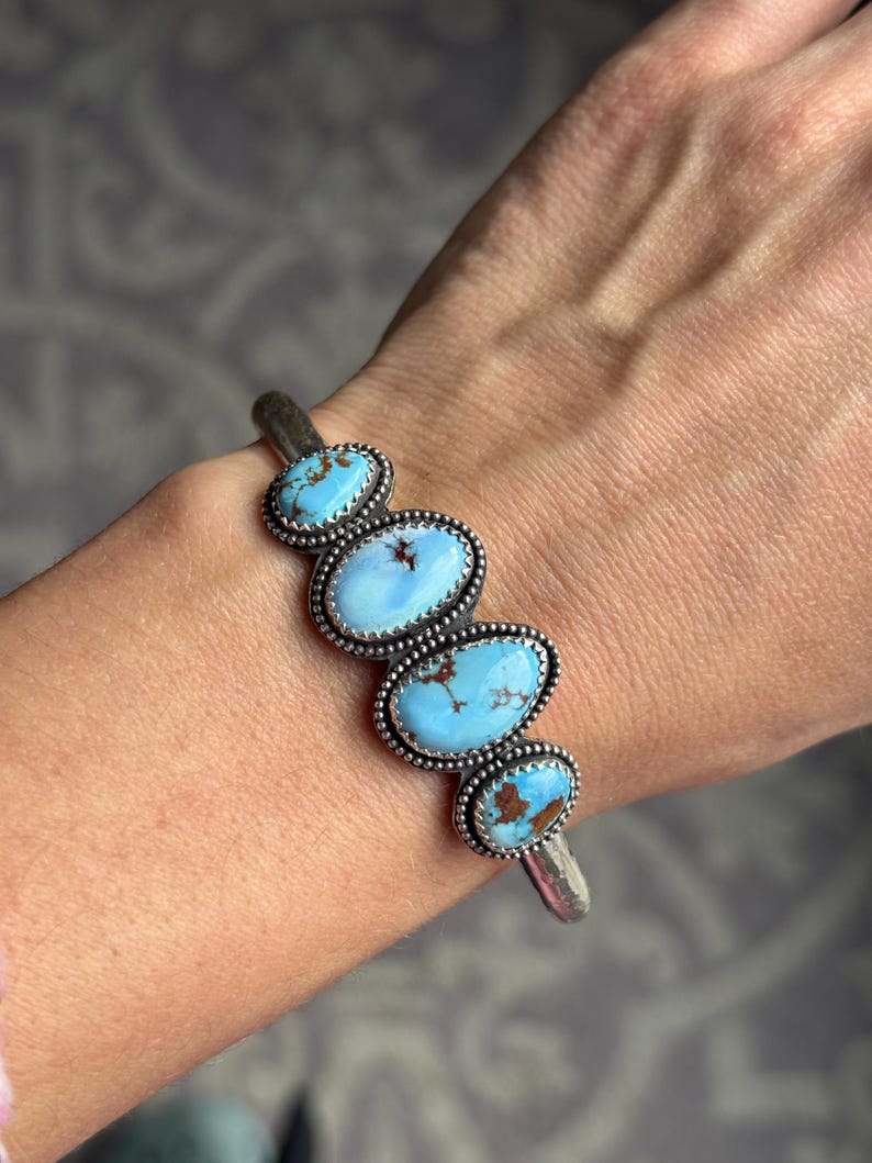 May include: Silver cuff bracelet featuring five oval turquoise stones. Each stone is a light blue color with brown matrix patterns, set in a beaded silver bezel. The bracelet is a classic southwestern style.
