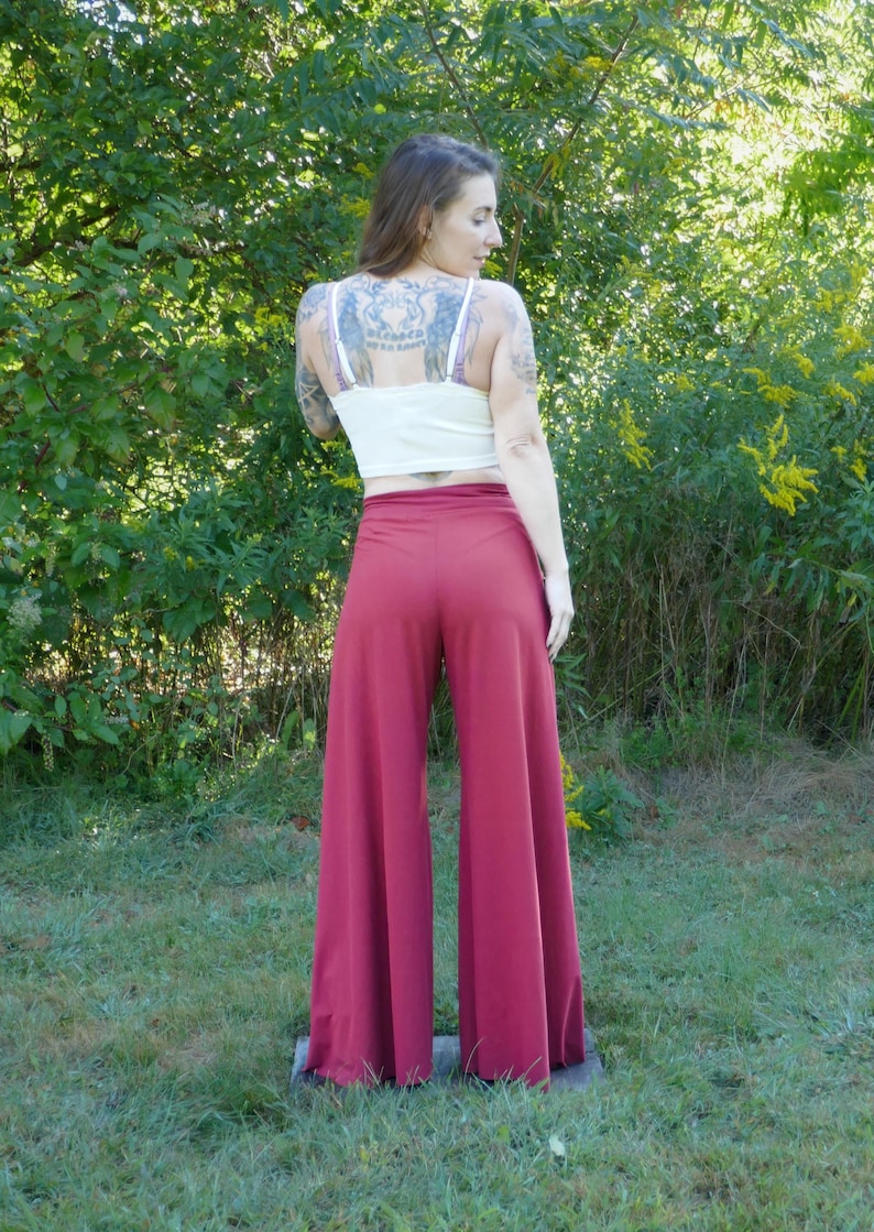 Puede incluir: Una mujer con un top blanco corto y pantalones anchos de color burdeos. Los pantalones tienen una cintura ancha y piernas anchas.