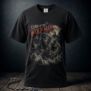 May include: A black short-sleeved t-shirt featuring a graphic print titled Curse of the Wolf-Man: A Tale of Gothic Lycanthropy. The illustration depicts a werewolf looming over a person in a dark, moonlit forest setting with a castle in the background.