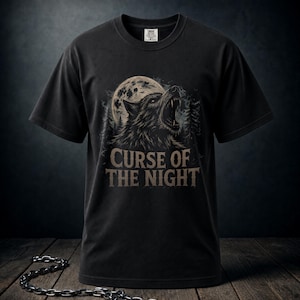 Può includere: Una t-shirt nera a maniche corte con la grafica di un lupo che ulula davanti a una luna piena e alla sagoma di un bosco. Il testo CURSE OF THE NIGHT è stampato in un carattere beige usurato sotto il lupo. Una catena metallica è in primo piano.