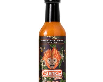May include: A clear glass bottle filled with orange hot sauce, topped with a black cap. The label features a monkey illustration, floral patterns, and the text Honey Mango Habanero Hot Sauce and Stanky Sauce, with a net volume of 5 fl. oz.