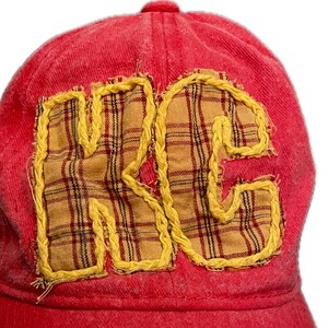 Pu&ograve; includere: Un cappellino da baseball rosso con le lettere "KC" applicate sul davanti. Le lettere sono realizzate in tessuto giallo con un motivo a quadri e bordate con cuciture gialle. Il cappellino &egrave; realizzato in un materiale morbido e strutturato.
