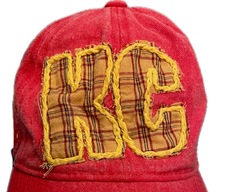 Pu&ograve; includere: Un cappellino da baseball rosso con le lettere "KC" applicate sul davanti. Le lettere sono realizzate in tessuto giallo con un motivo a quadri e bordate con cuciture gialle. Il cappellino &egrave; realizzato in un materiale morbido e strutturato.