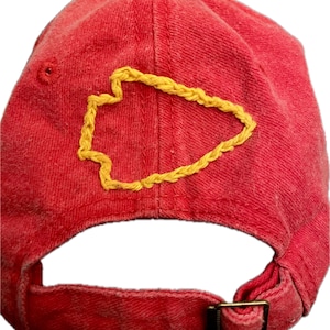 Pu&ograve; includere: Cappellino da baseball rosso con un design a punta di freccia gialla ricamato. Il cappellino ha una visiera curva, un cinturino regolabile e una fibbia in metallo. Il tessuto &egrave; morbido e usurato.