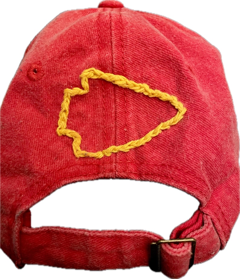 Pu&ograve; includere: Cappellino da baseball rosso con un design a punta di freccia gialla ricamato. Il cappellino ha una visiera curva, un cinturino regolabile e una fibbia in metallo. Il tessuto &egrave; morbido e usurato.