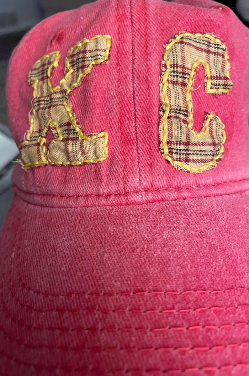 Pu&ograve; includere: Un cappellino da baseball rosa con le lettere "KC" applicate sul davanti. Le lettere sono realizzate in tessuto a quadri con cuciture gialle. Il cappellino &egrave; realizzato in un materiale morbido e strutturato.