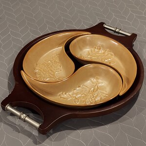 May include: A brown wooden serving tray with three beige ceramic bowls. The bowls are shaped like yin and yang symbols and have a leaf design.