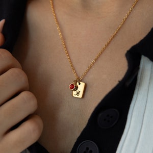 May include: A gold chain necklace with a small square pendant featuring the letter "R" and a red gemstone.