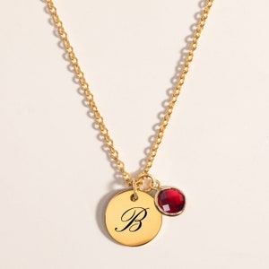 Peut inclure: Collier en or avec un pendentif rond orné de la lettre 'B' en écriture cursive. Une petite pierre rouge pend du pendentif.