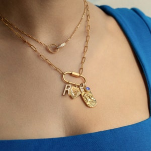 Gold paperclip chain necklace with customizable charms, featuring a cubic zirconia-studded 'R,' personalized engraved tag, Aquarius zodiac charm with textured detail, and September birthstone blue gem. A unique, personalized gift option.