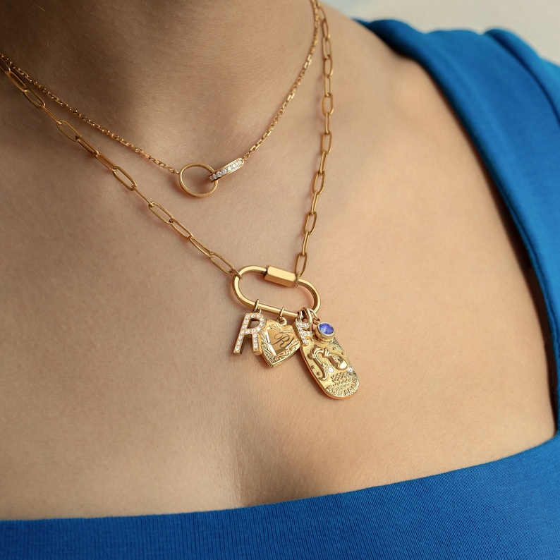 Gold paperclip chain necklace with customizable charms, featuring a cubic zirconia-studded 'R,' personalized engraved tag, Aquarius zodiac charm with textured detail, and September birthstone blue gem. A unique, personalized gift option.