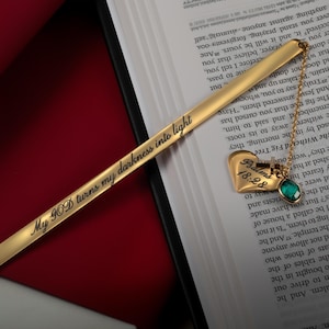 May include: A gold bookmark with the inscription "My GOD turns my darkness into light" and a heart-shaped charm with the words "Psalms 18:28" and a green gemstone.