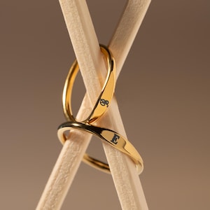 Peut inclure: Deux anneaux en or entrelacés, l'un gravé de la lettre "E" et l'autre de la lettre "S". Les anneaux reposent sur deux bâtonnets en bois.