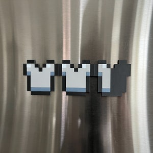 May include: A set of three pixelated magnets in the shape of a crown. The crowns are gray with blue accents and black outlines. The magnets are arranged in a row.