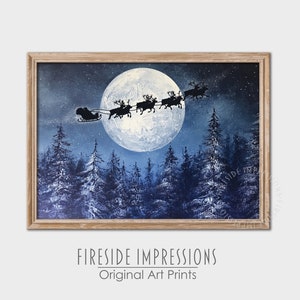 May include: A framed art print depicts Santa's sleigh pulled by reindeer silhouetted against a full moon in a winter forest. The artwork is set against a dark blue sky with a light brown wooden frame. The text "Fireside Impressions Original Art Prints" is at the bottom.