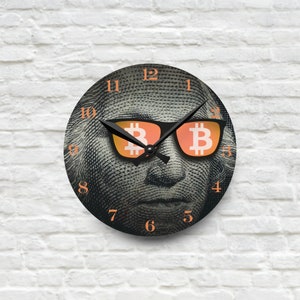 May include: A black clock with a white face and black hands. The face of the clock is a close-up of a man's face with sunglasses. The sunglasses have the Bitcoin symbol on the lenses.