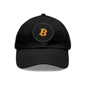 Puede incluir: Una gorra de béisbol negra con un parche redondo negro que presenta un símbolo de Bitcoin naranja.