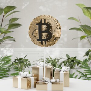 May include: A gold balloon shaped like a Bitcoin symbol, with a black Bitcoin symbol inside, is floating above three gold gift boxes with white ribbon bows.