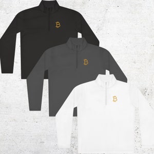 May include: Three quarter-zip pullover shirts in black, grey, and white with a gold Bitcoin symbol embroidered on the chest.