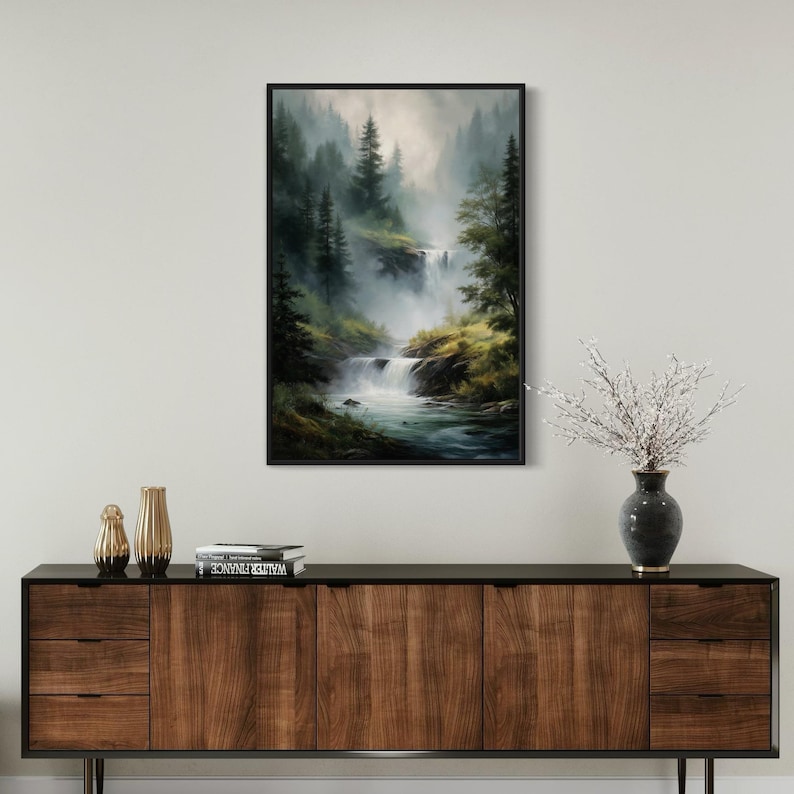 May include: A framed painting of a misty forest scene with a waterfall cascading down a rocky hillside. The painting is in a black frame and is hanging on a white wall.