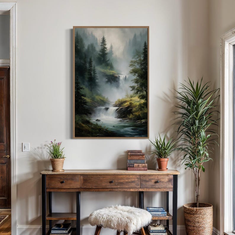 May include: A framed painting of a misty forest scene with a waterfall flowing through it. The painting is in a wooden frame and is hanging on a white wall.