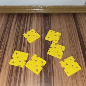 May include: Five small, square, bright yellow plastic pieces designed to resemble slices of Swiss cheese, each featuring multiple irregular cutouts and holes of varying sizes scattered across their flat, textured surfaces.
