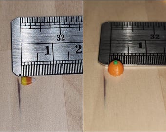 May include: Two small candy decorations, a candy corn and a pumpkin, are measured against a ruler. The candy corn is about 1/2 inch long and the pumpkin is about 1/4 inch tall.