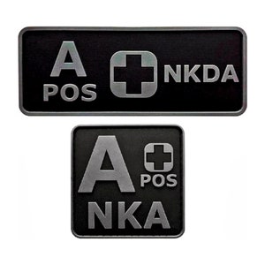 May include: Two black rectangular patches with white text and a silver cross. The top patch reads "A POS NKDA" and the bottom patch reads "A POS NKA".