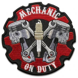 May include: Embroidered patch with a black border, featuring a red gear shape. The patch displays the word "MECHANIC" in white arched text above a design of crossed wrenches, pistons, and a spark plug. The text "ON DUTY" is below.