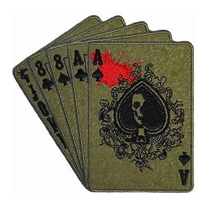 May include: A set of five playing cards, all spades, with a skull and crossbones design on the ace of spades. The cards are green with black embroidery and a red blood splatter on the ace.