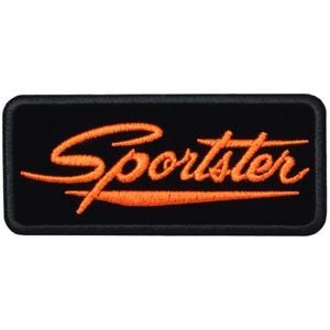 May include: Black rectangular patch with the word "Sportster" embroidered in orange script. A matching orange line underlines the word. The patch has a black border.
