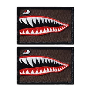 May include: Two brown fabric patches with black stitching, each featuring a white and red embroidered image of a shark's mouth with sharp teeth.