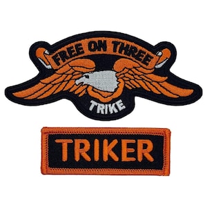 May include: Two embroidered patches, one with an eagle and the text "Free On Three Trike" and the other with the text "Triker" in orange letters on a black background.