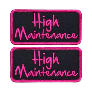 May include: Two black rectangular patches with pink embroidered borders. The text "High Maintenance" is embroidered in pink on each patch.