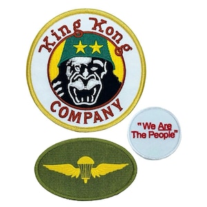 May include: Three embroidered patches. The first is round and features a cartoon gorilla wearing a green army hat with two stars. The text "King Kong Company" surrounds the gorilla. The second patch is round and white with red text that reads "We Are The People". The third patch is oval and green with a yellow parachute and wings.