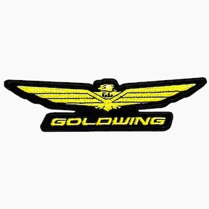 May include: Black and yellow embroidered patch featuring a stylized wing design with the word "GOLDWING" in yellow text. The patch has a black border and is likely for a jacket or bag.