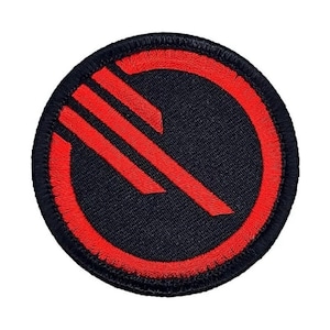 May include: A black and red embroidered patch with a red symbol of a circle with a diagonal line through it. The symbol is surrounded by a red circle.