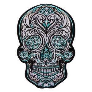 May include: A black and white embroidered sugar skull patch with turquoise details. The skull is decorated with intricate floral patterns and swirls.