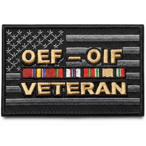 May include: A rectangular black patch with an embroidered American flag design. The patch features the text "OEF-OIF VETERAN" in gold lettering, with a row of colorful ribbons below the text. The flag design is in black and white.