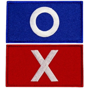 May include: Two rectangular patches: one blue with a white circle, the other red with a white X. The patches are embroidered with a textured appearance, suitable for sewing onto clothing or accessories. The design is simple and graphic.