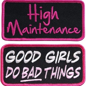 May include: Two black fabric patches with pink stitching. The top patch says "High Maintenance" in pink lettering. The bottom patch says "Good Girls Do Bad Things" in white and pink lettering.