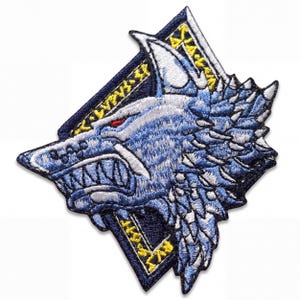 May include: An embroidered patch featuring a stylized wolf head in shades of blue, white, and grey with a red eye. The wolf is set against a dark blue diamond-shaped background with yellow runic-style symbols along the top and bottom edges.