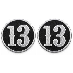May include: Two circular patches with the number 13 in a decorative font. The patches have a black background with a white border and white number. The patches are likely for clothing or accessories.