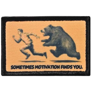 May include: A rectangular patch with a black border features a sepia-toned image of a person running from a bear. The text "SOMETIMES MOTIVATION FINDS YOU" is printed in white at the bottom of the patch.