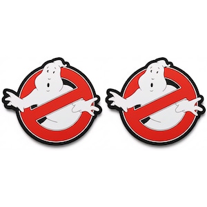 May include: Two identical Ghostbusters logo decals. Each features a white ghost figure inside a red circle with a diagonal red line, all outlined in black. The ghost has an open-mouthed expression and outstretched arms.