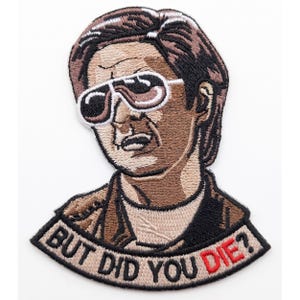 May include: An embroidered patch featuring a person with brown hair wearing white-rimmed sunglasses. The person wears a brown jacket over a white shirt. Below the figure, a banner contains the black text "BUT DID YOU" and the red word "DIE?".