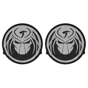 May include: Two black and silver embroidered iron-on patches featuring a Predator head with dreadlocks and a symbol on the forehead.