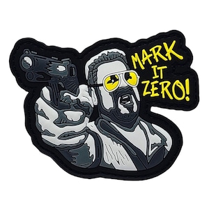May include: A black, gray, and white patch featuring a man with yellow-tinted sunglasses pointing a gun. The text "MARK IT ZERO!" is in yellow. The patch has a black border.