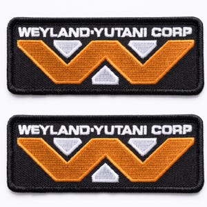 May include: Two rectangular black embroidered patches. Each patch features the text "WEYLAND-YUTANI CORP" in white, above a stylized orange and white "W" design. The patches are likely for clothing or accessories.